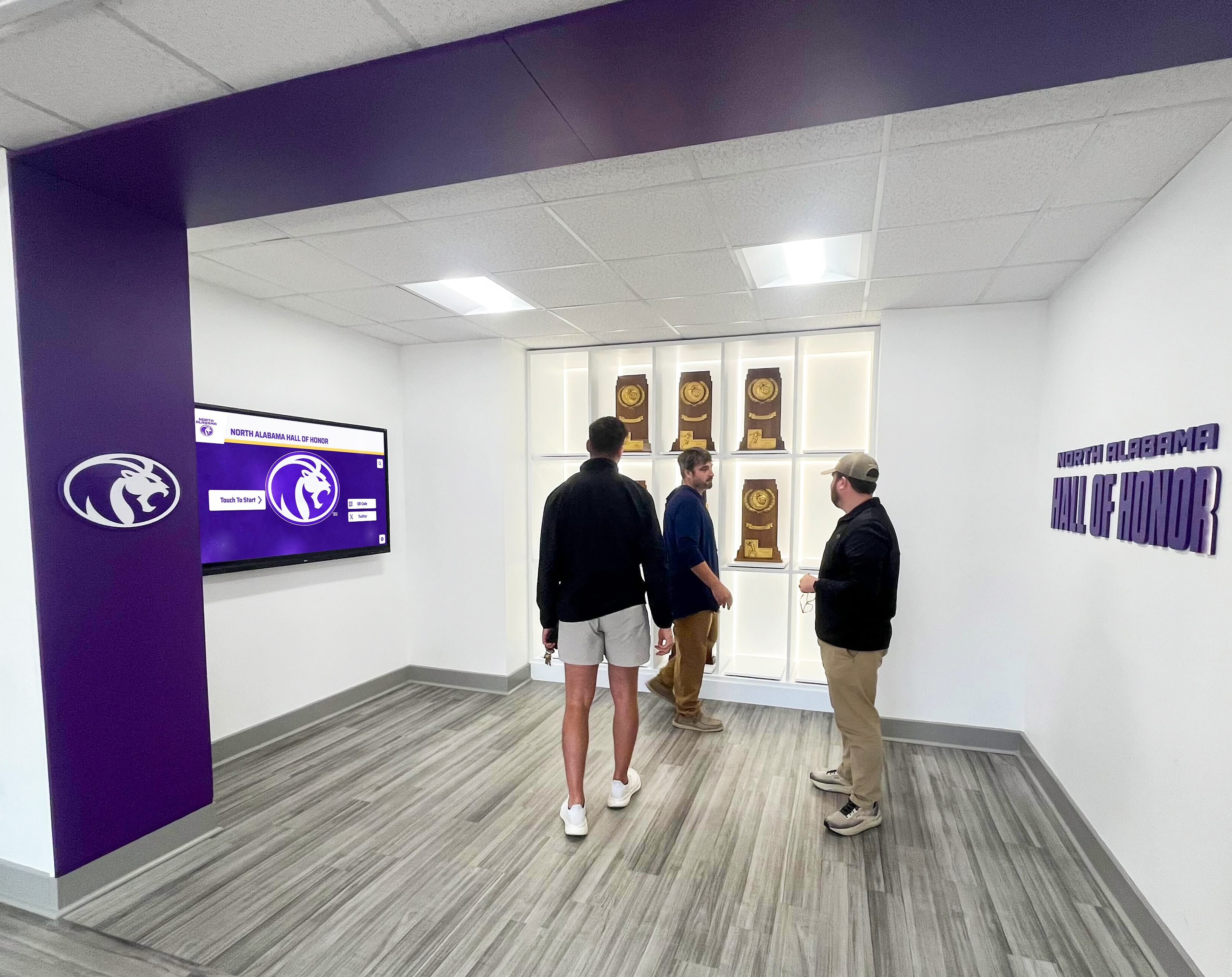 Visitors exploring athletic hall of honor with trophy displays Multiple people viewing athletic display