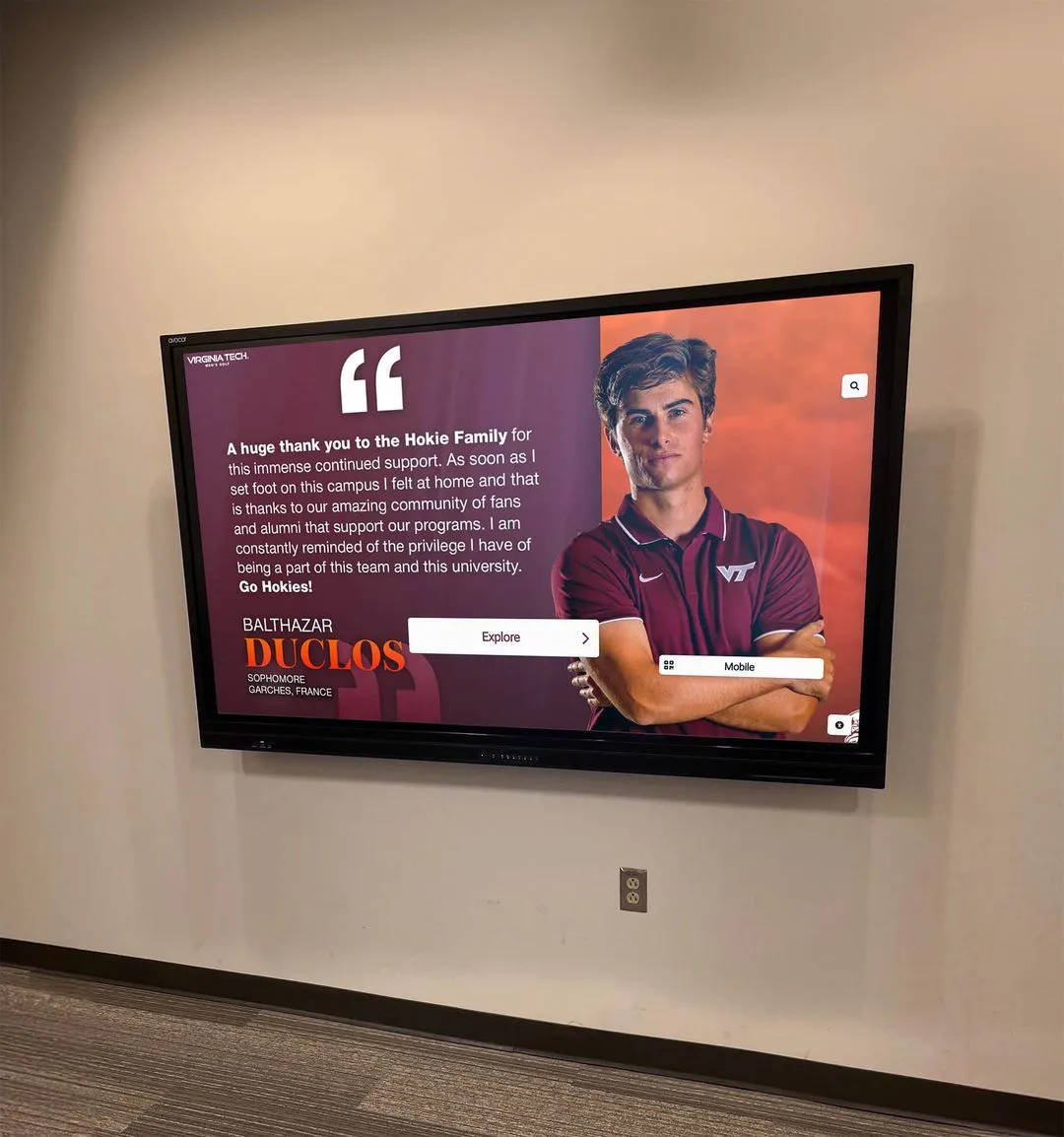 Virginia Tech student athlete pointing at maroon-branded wall display
